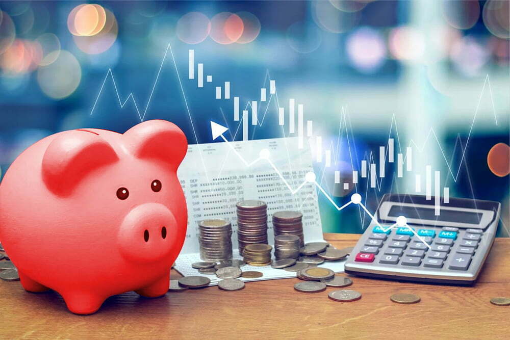 A red piggy bank, stacks of coins and a calculator under an overlaid candlestick chart
